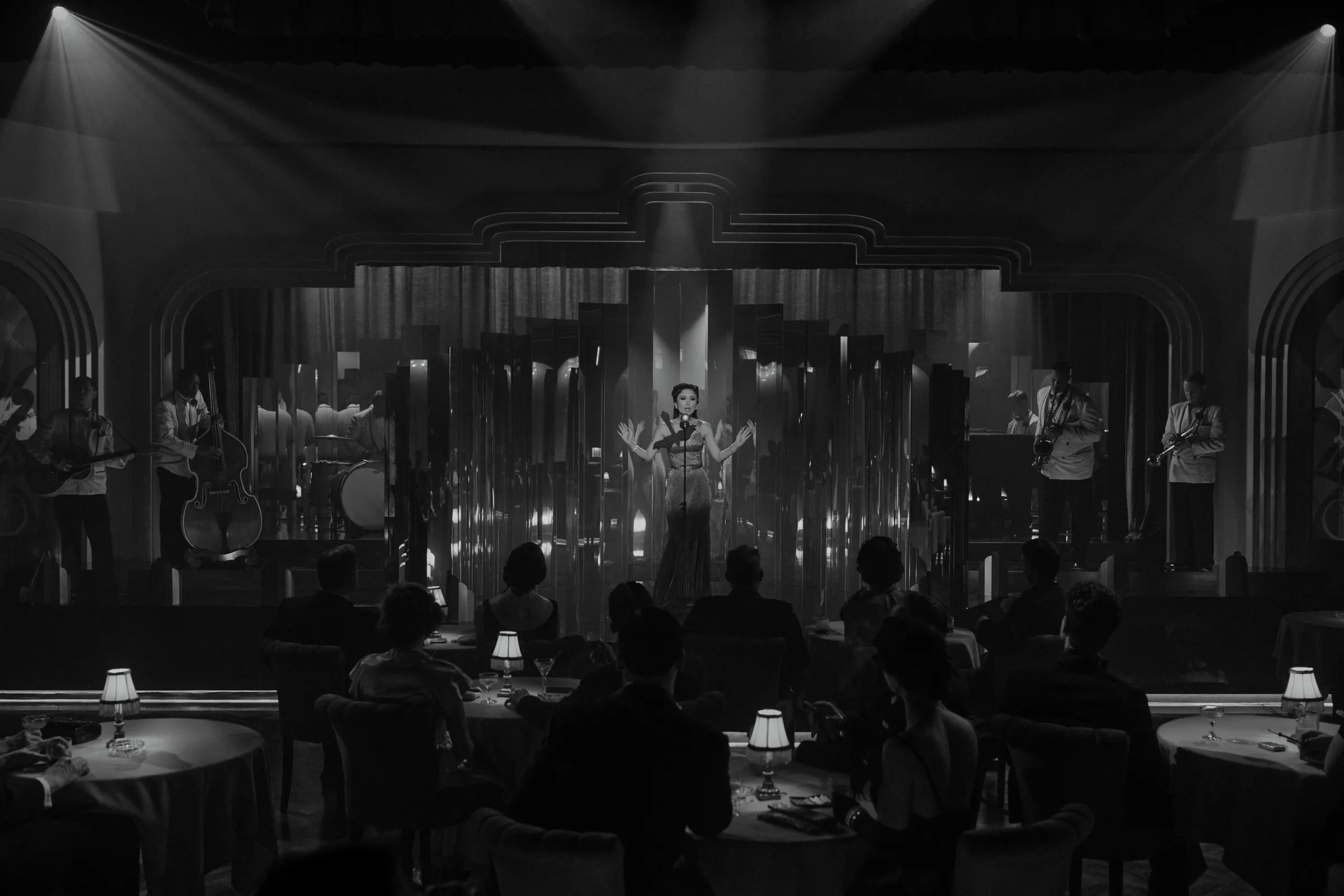 A black and white image of a woman singing on stage before a crowd in a night club.