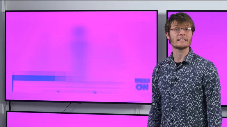 A woman in a blue shirt looks t a colorful OLED screen in a dark room..