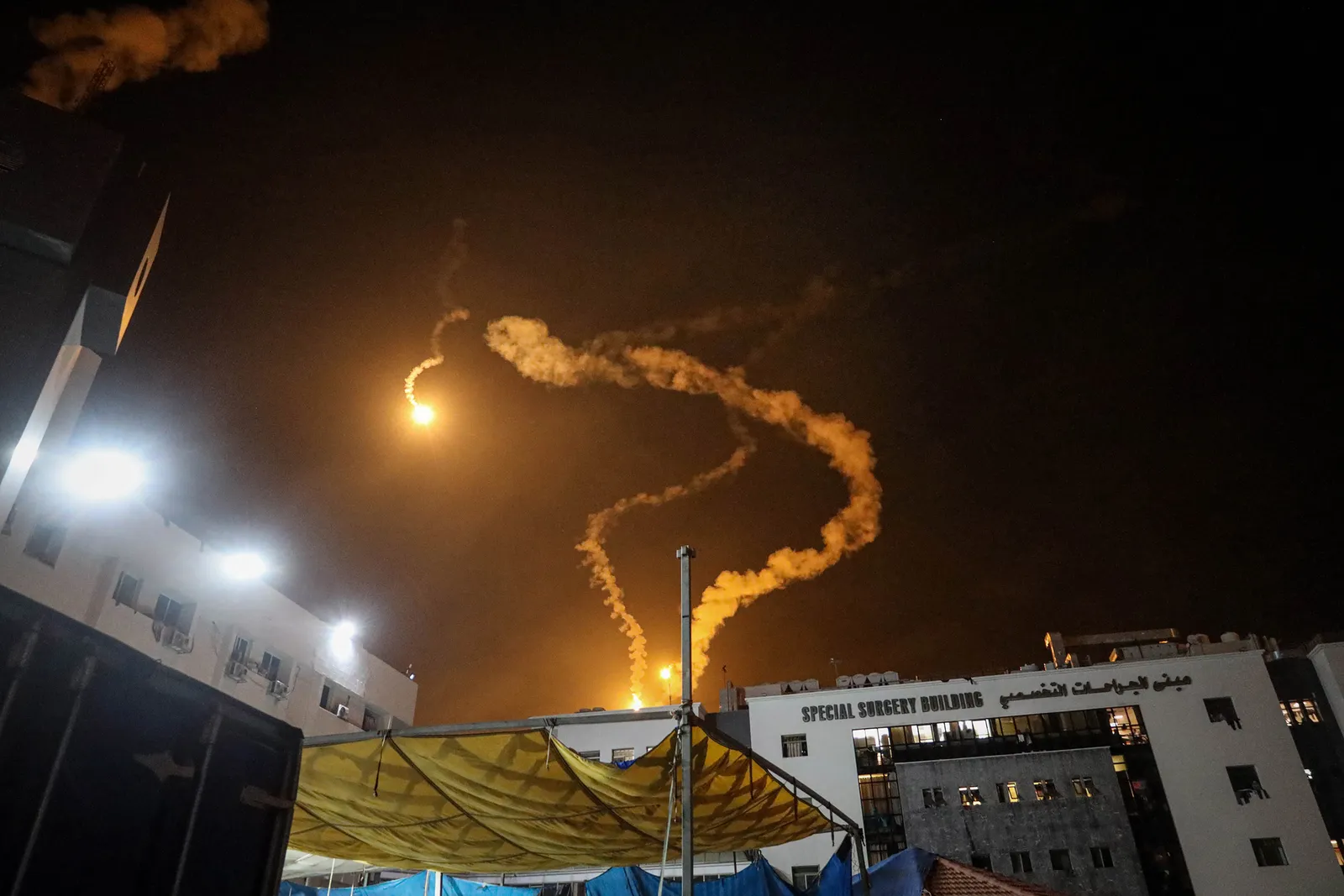 Aerial view of people crowded outside of AlShifa hospital with a smoke cloud in the distance