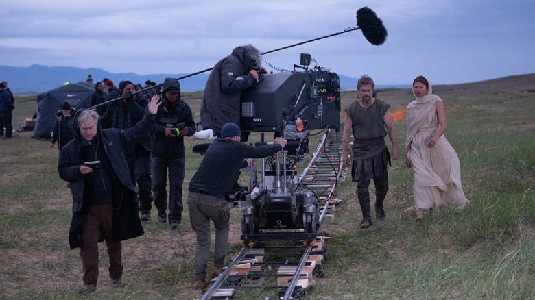A behind the scenes photo shows Christopher Nolan directing the Odyssey with large IMAX camera and actors Zendaya and Matt Damon