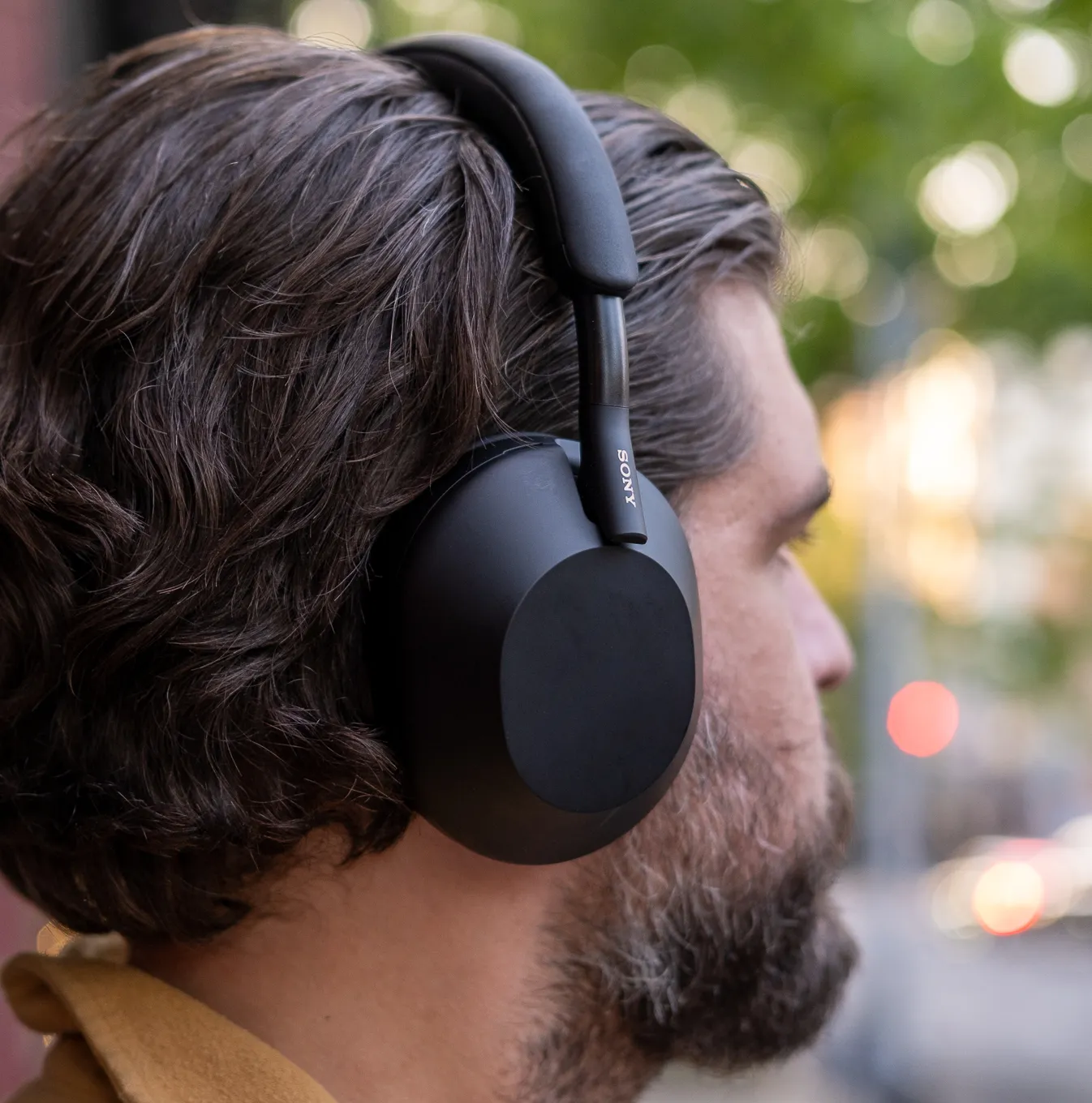 A man wearing Sony’s black WH-1000XM5 noise-canceling headphones outside.
